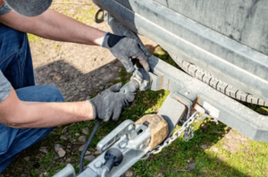 Mechanic connecting trailer plug and inspecting safety chains before a trailer safety certificate inspection on the Sunshine Coast
